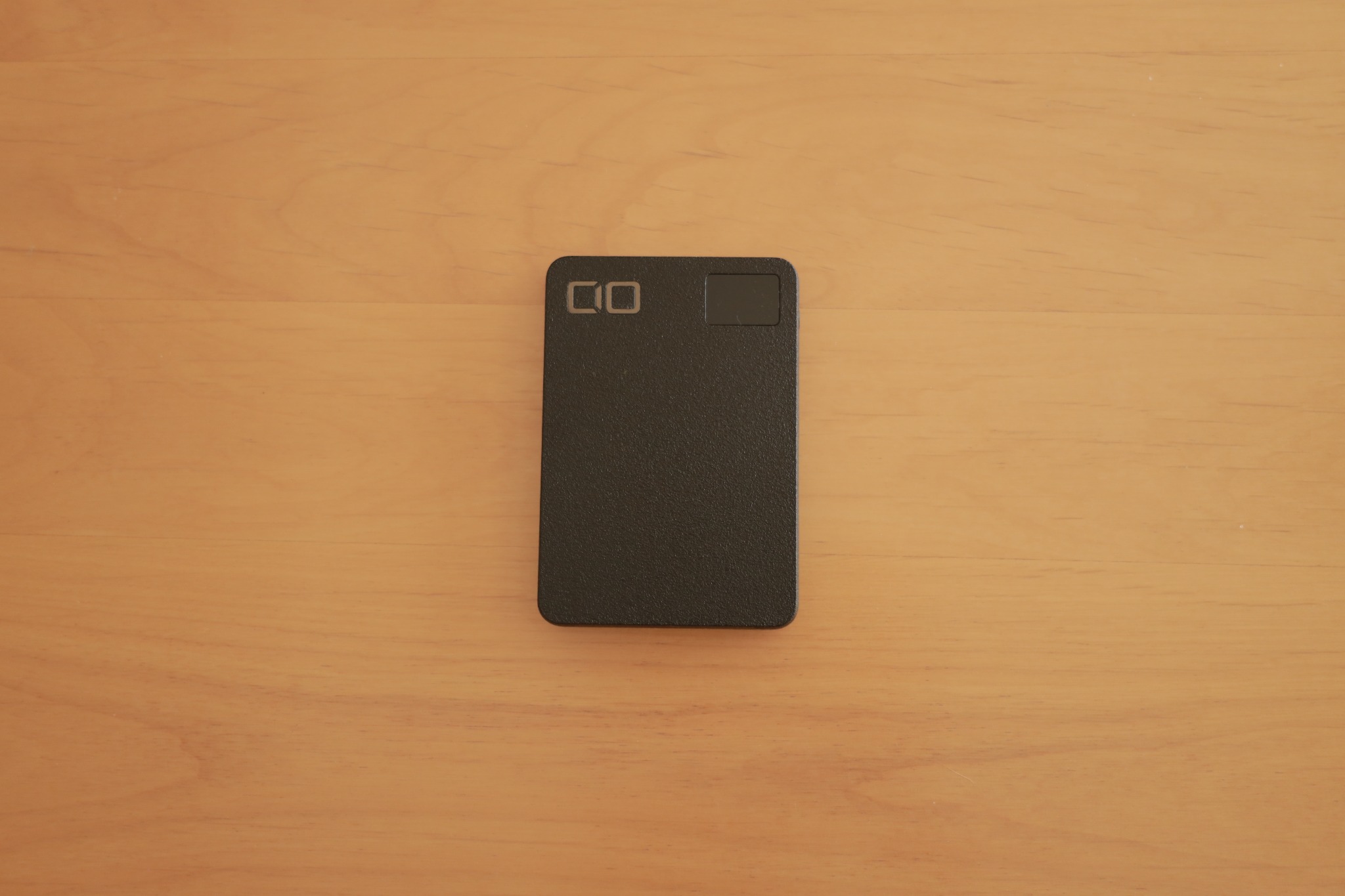 木のテーブルに置いた黒いCIO SMARTCOBY SLIMの正面写真。ロゴと残量表示部が見える