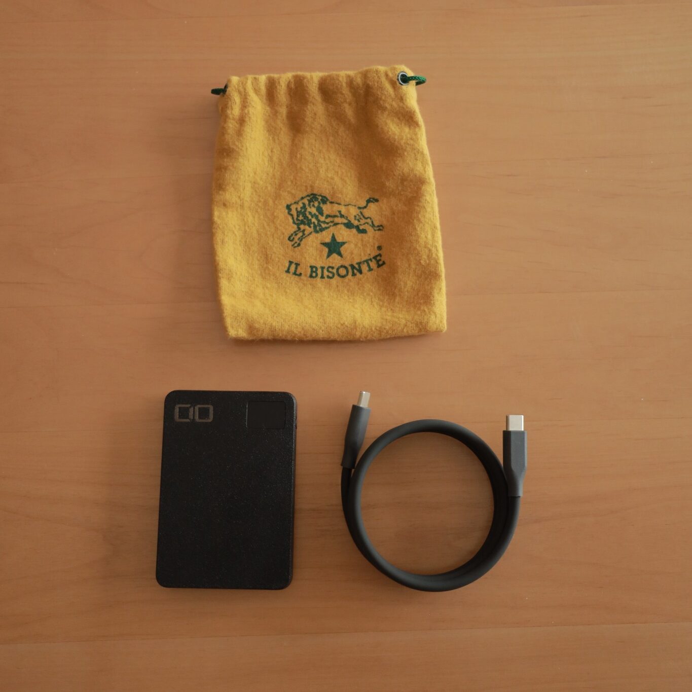 木のテーブルにCIO SMARTCOBY SLIM、USB-Cケーブル、黄色い巾着を並べた写真