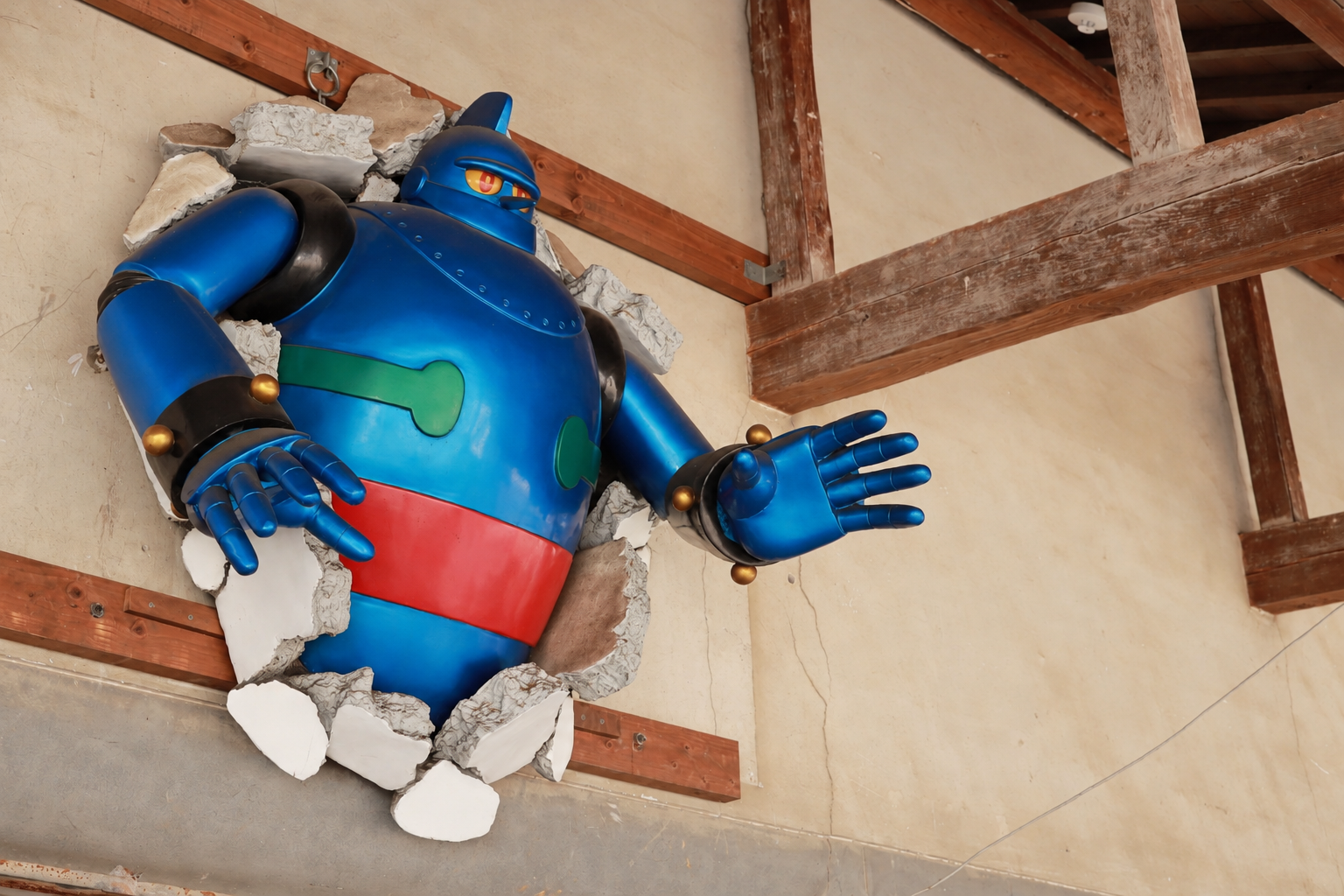木の梁と壁の間から身を乗り出す、大きな青いロボットの展示