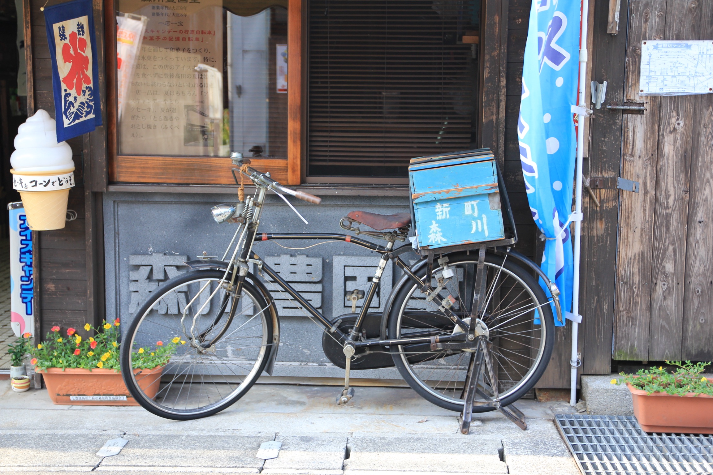 木の店先に置かれた昔ながらの自転車と青い荷箱、アイスの看板